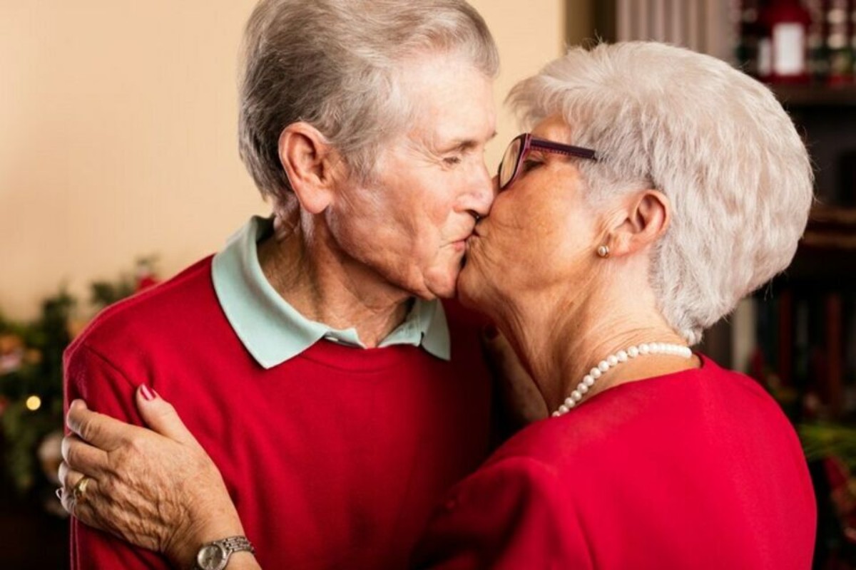 Un couple âgé partage un baiser tendre, vêtu de rouge, symbole d’amour éternel et de complicité après 70 ans de mariage – Illustration des noces de platine.
